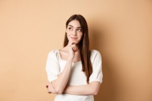 A imagem mostra o rosto de uma mulher branca, com cabelos loiros, compridos e ondulados, e olhos azuis. Ela olha para a frente e está sobre um fundo cinza.